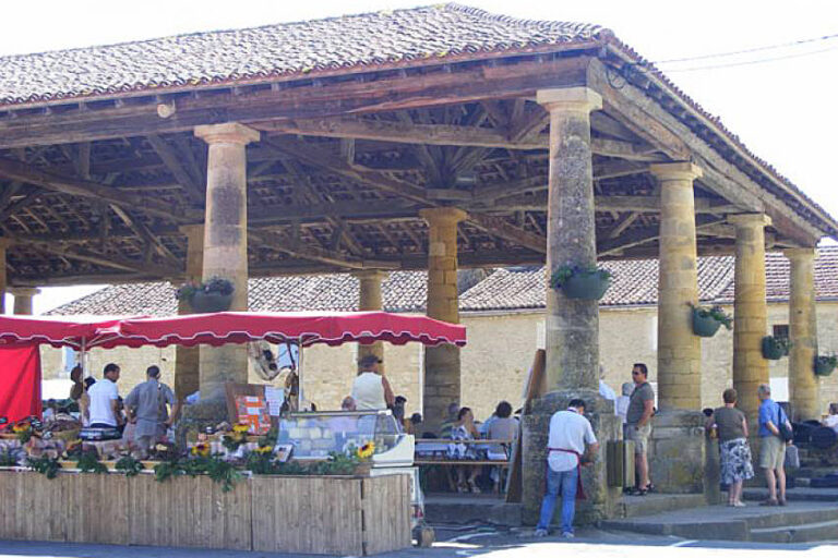 Shoppers browsing merchandise under the traditional wooden beamed Market Halle roof structure in Villefranche-du-Perigord